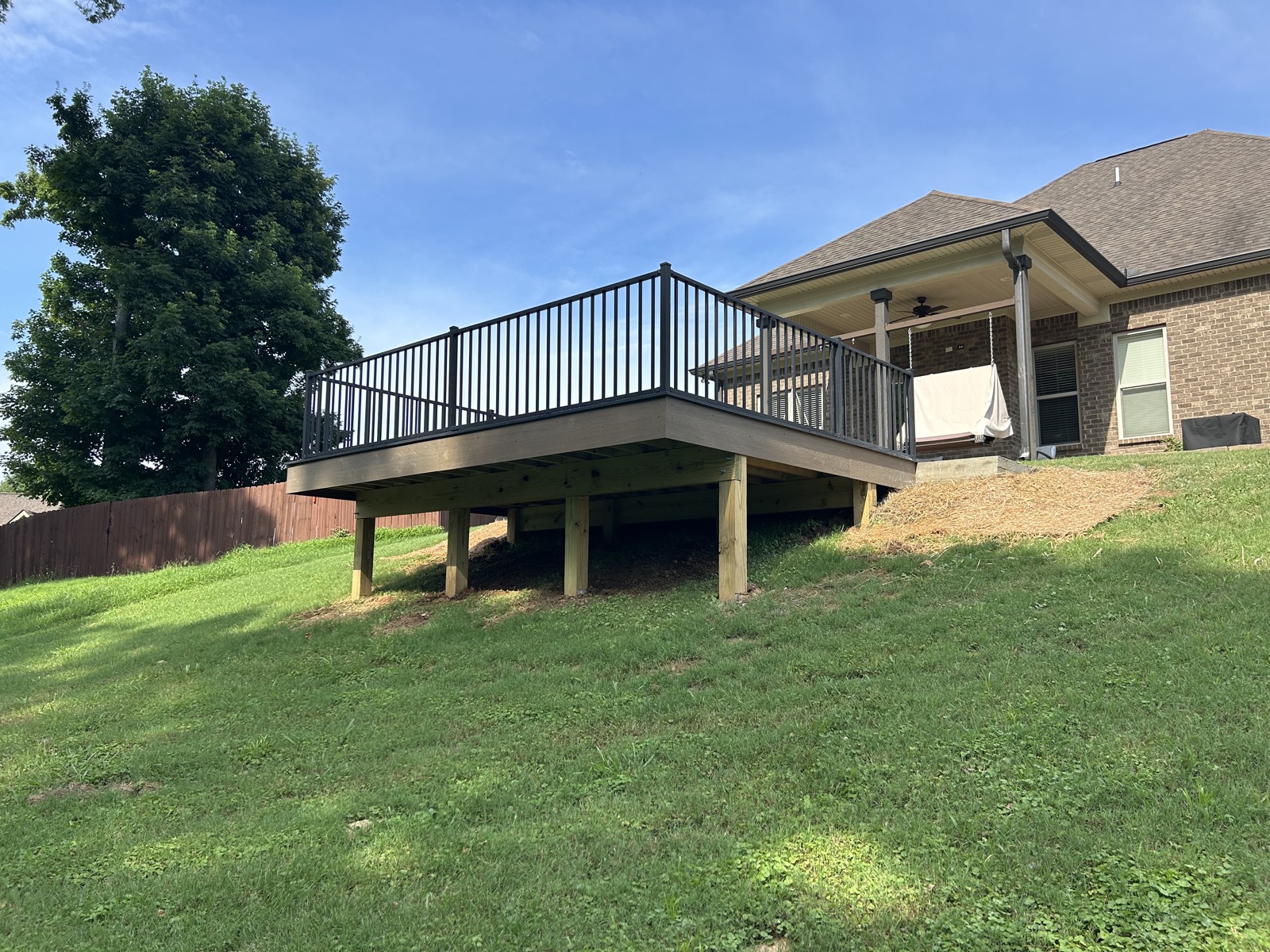 Elevated deck with a covered porch and black metal railing on a brick home
