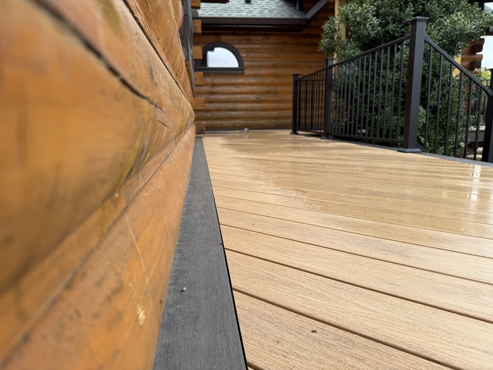 Warm composite decking beside a log home with black aluminum railing