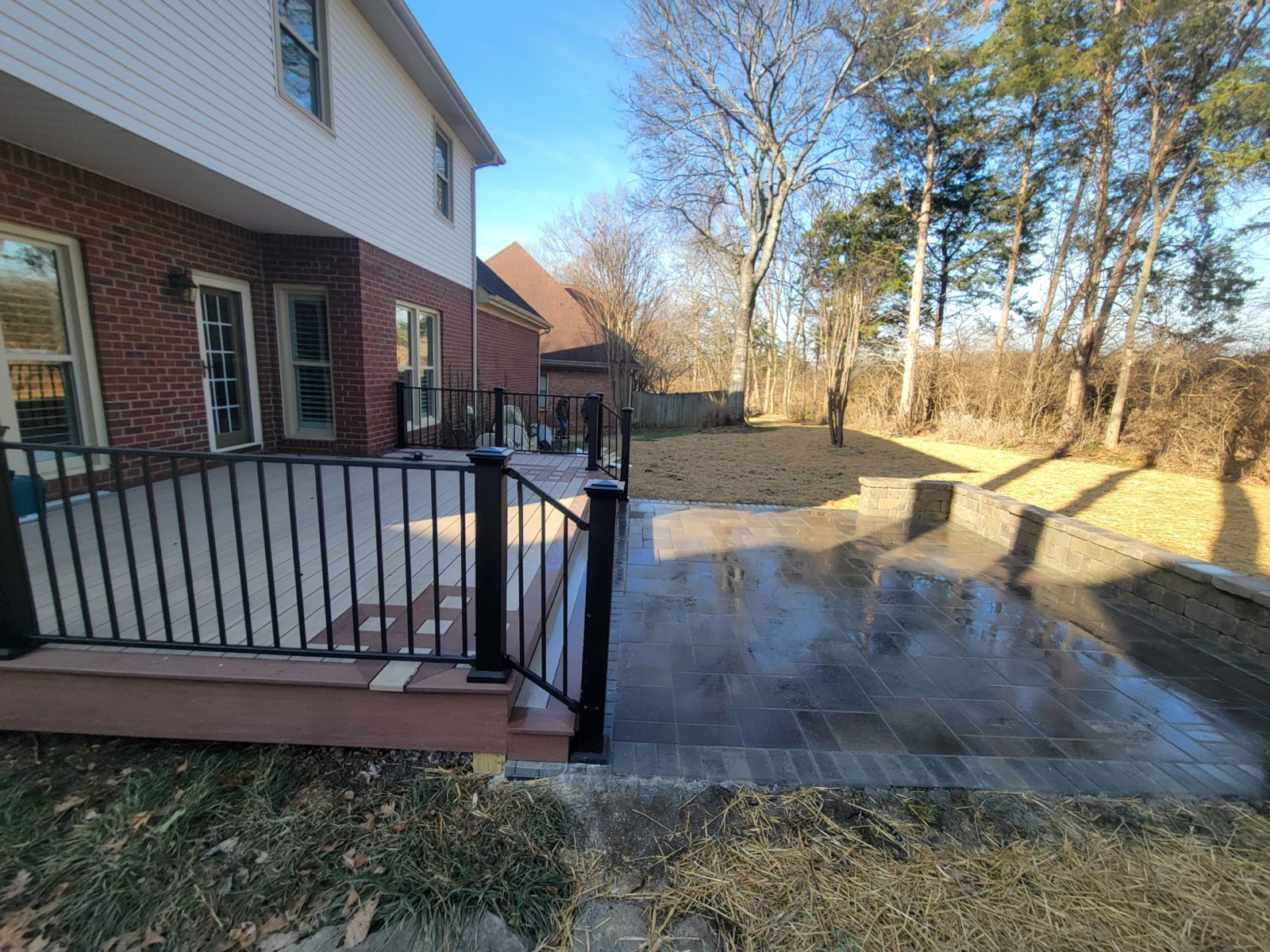Composite deck flowing into an expansive paver patio across the backyard