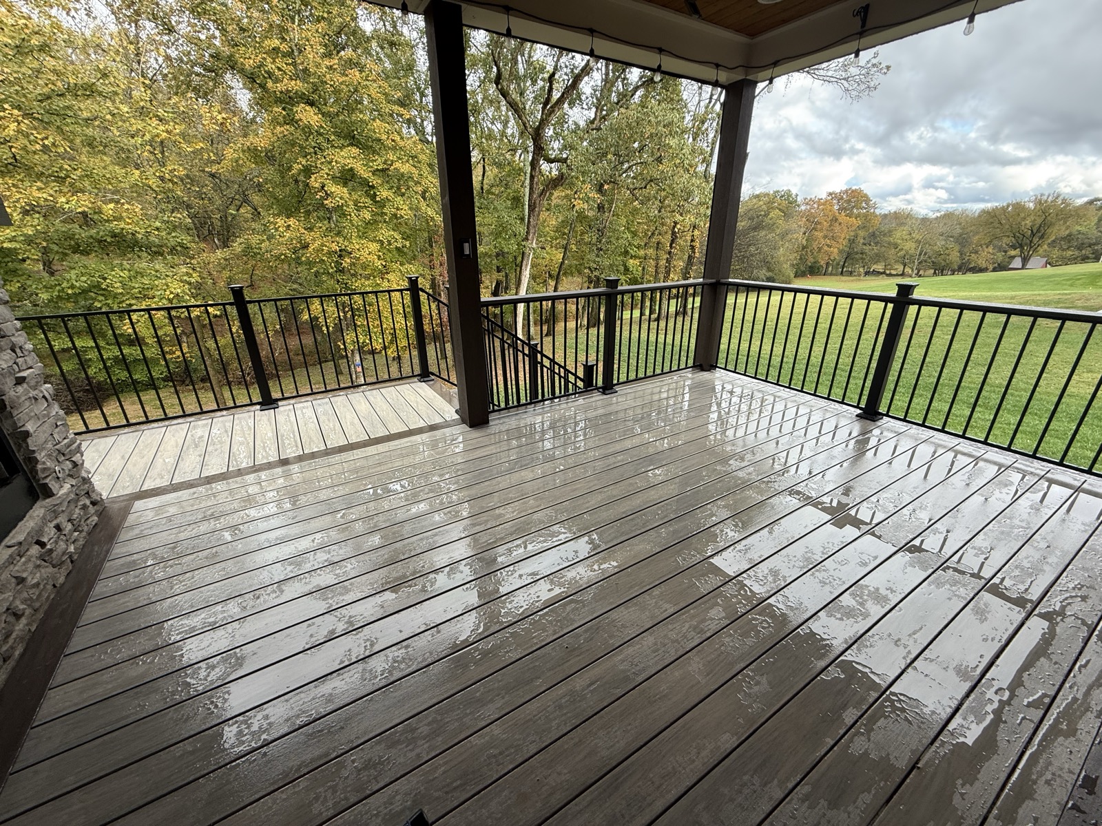 Covered composite porch with black railing overlooking autumn trees and lawn