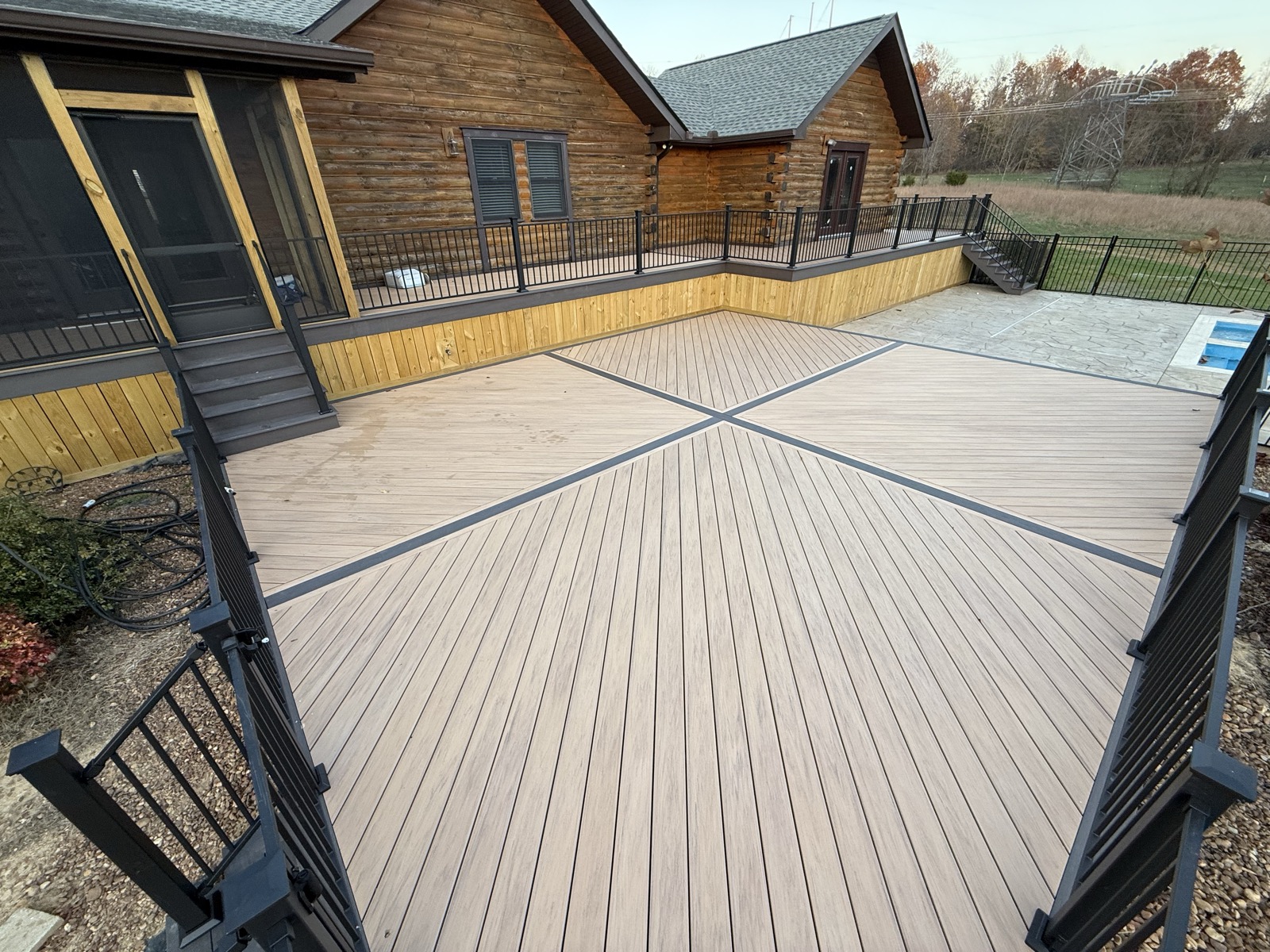 Composite deck with picture-frame inlay pattern beside a pool at a log home