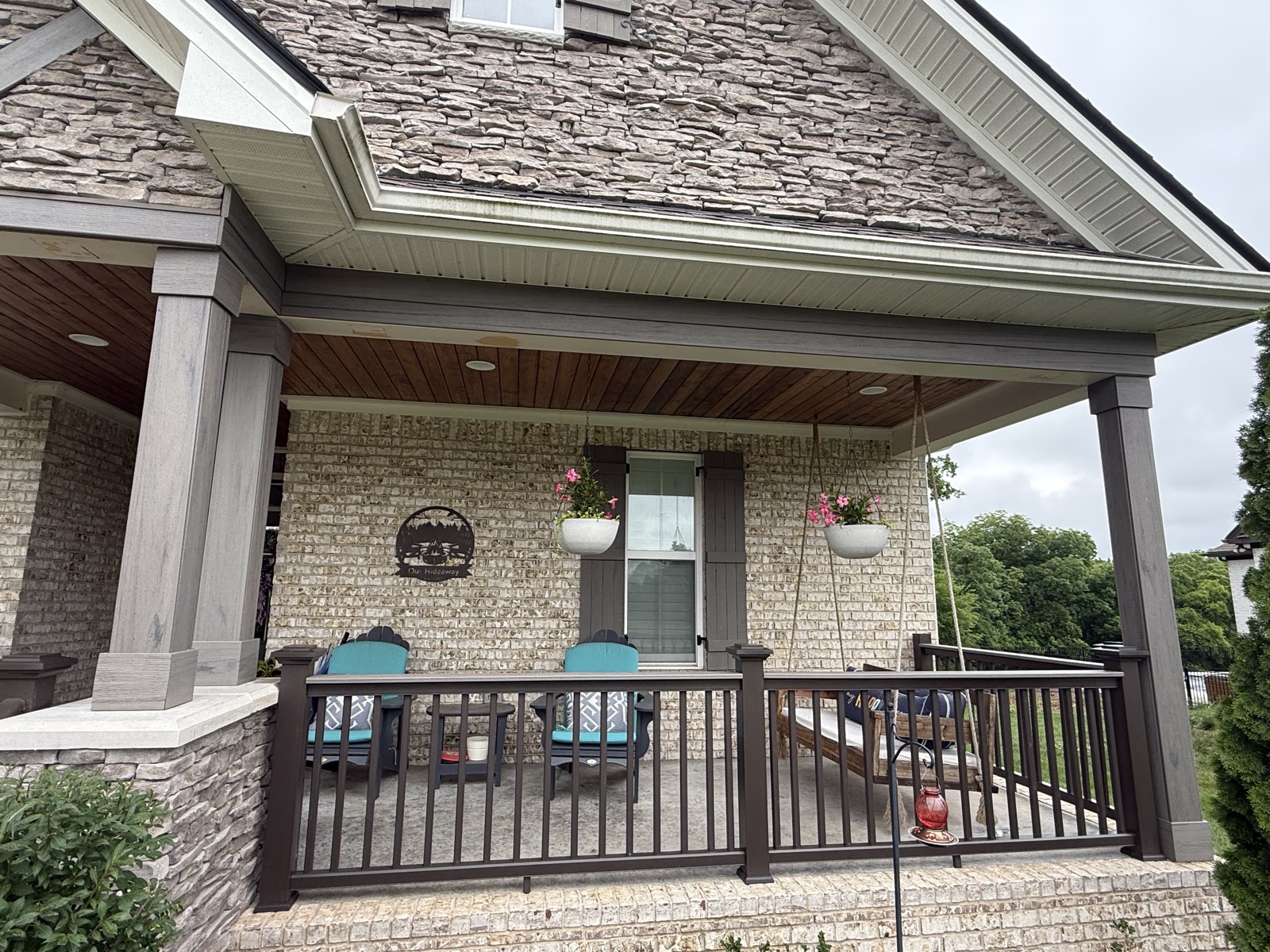 Covered porch with stone columns, black railing and seating on a brick home