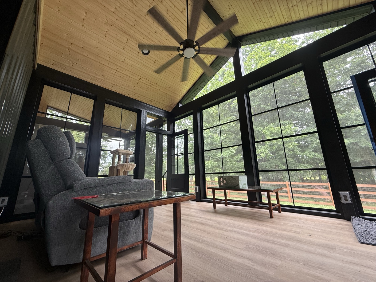Interior of an enclosed three-season room with vaulted wood ceiling and black-framed windows